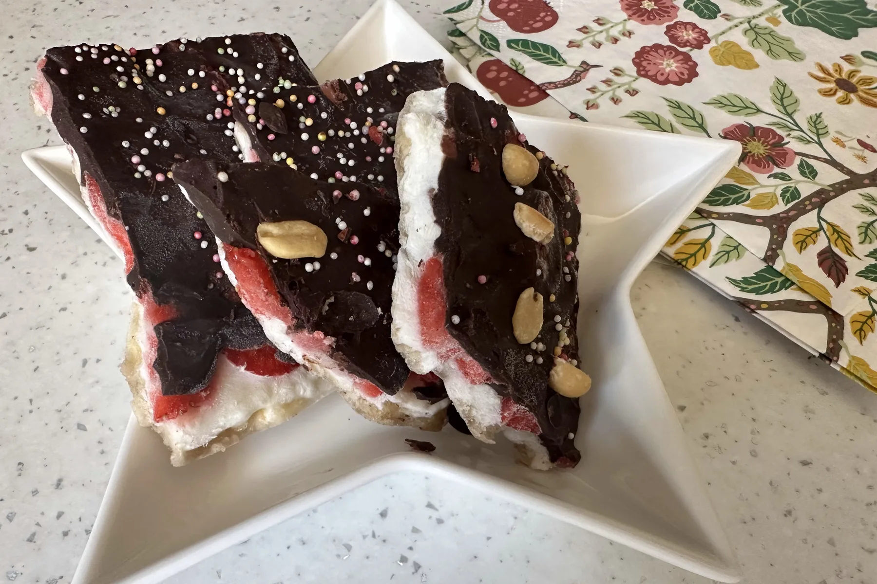 Broken shards of banana split bark on a star-shaped plate, showing the chocolate, yoghurt, strawberry and banana layers, topped with peanuts and sprinkles