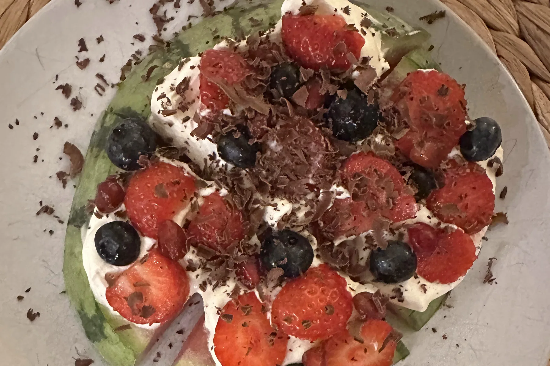 Watermelon pizza sliced into wedges, topped with whipped cream, strawberries, blueberries and grated dark chocolate
